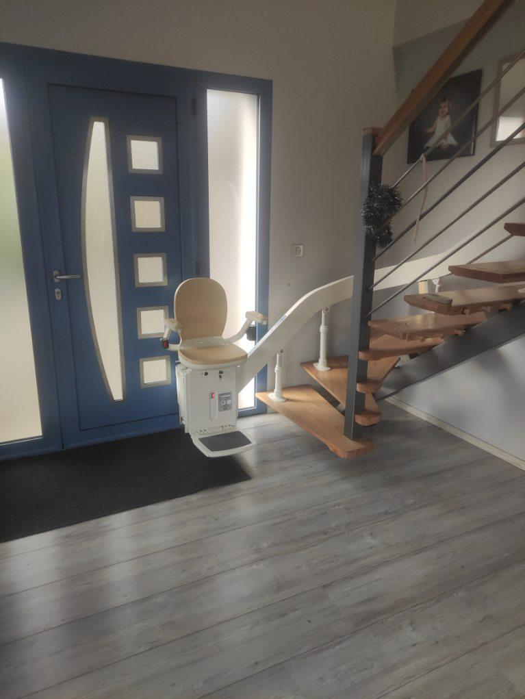 Monte-escaliers courbe avec rail escamotable en position basse, de coloris beige avec accoudoir et repose-pieds refermé