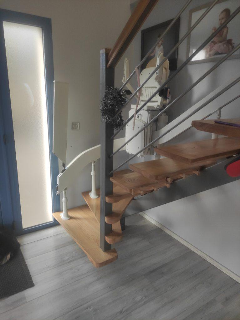Monte-escaliers courbe avec rail escamotable, de coloris beige en action avec accoudoir et repose-pieds refermé